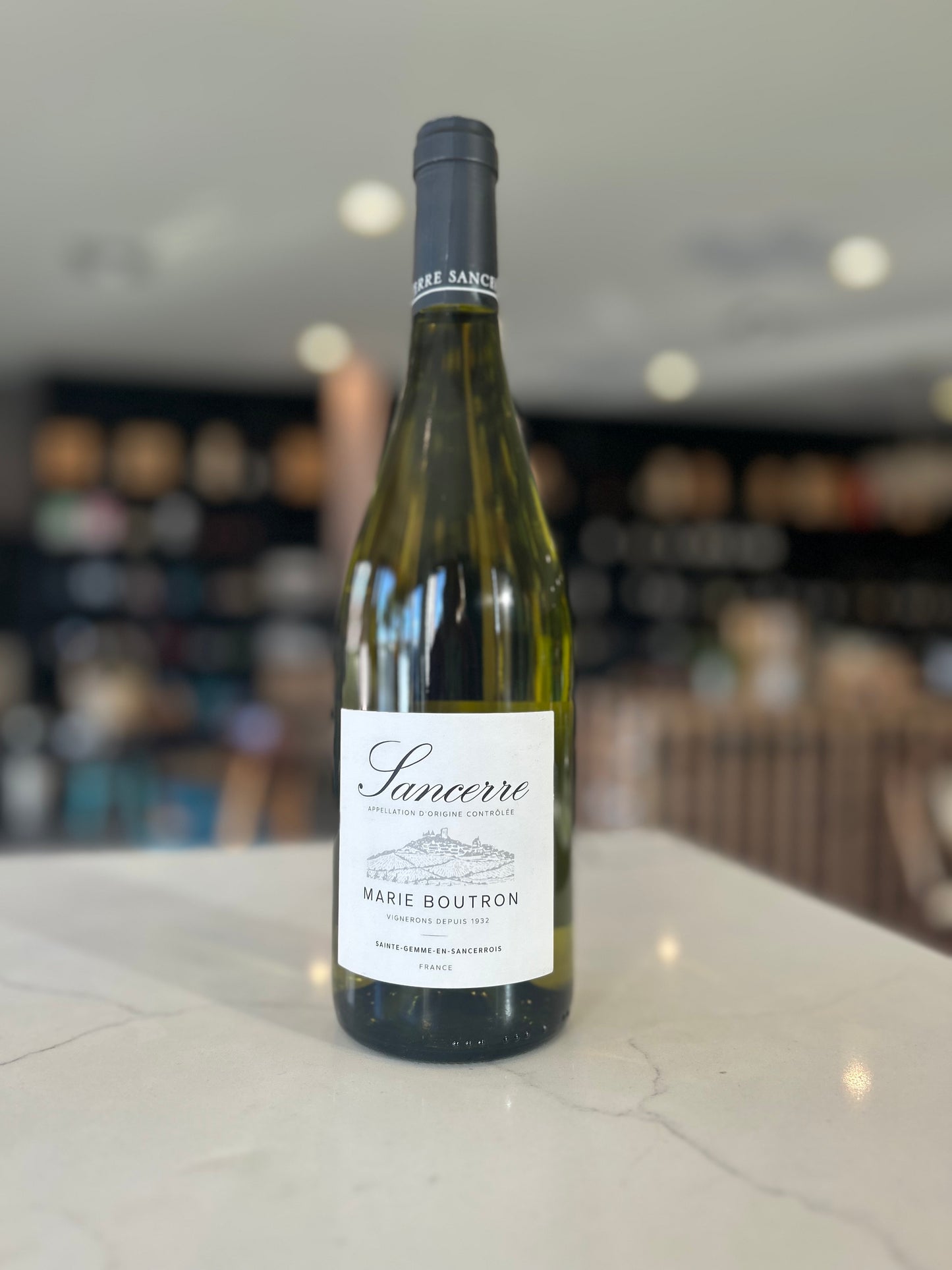 A bottle of Sancerre white wine by Marie Boutron, produced by Cap de Sangre, standing on a light marble countertop with a blurred indoor background.